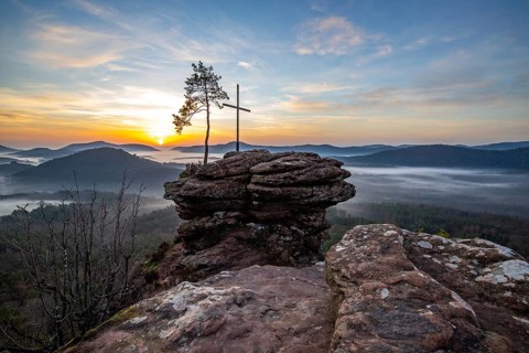 Landscape shot of nature in the morning. Mist in the valley and a summit cross on a sandstone cliff
