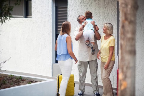 Grandfather greeting his young grandchild lifting him in the air and kissing him as he arrives on a