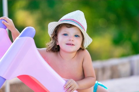 Baby kid girl with hat in summer on green field background