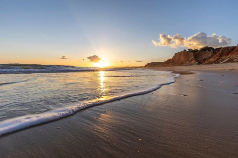 Beautiful sandy beach with red rocks and cliffs. Twilight at sunset with shallow waves on the