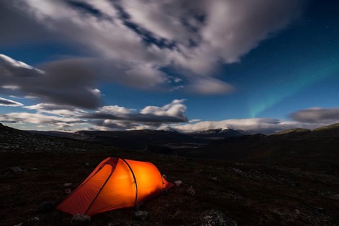 Northern Lights (Aurora borealis) over illuminated tent, Rapadalen, Sarek National Park, Laponia