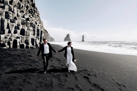 Destination Iceland wedding. A wedding couple walks along the sandy black beach of Vik, near the