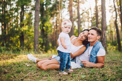 Little girl one year on the background of parents resting on graß learning to walk on nature in the