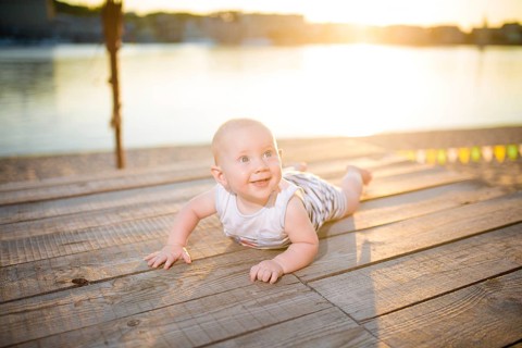A child a boy, one year old, blond man lies on his stomach on wooden dock, pier in striped clothes,