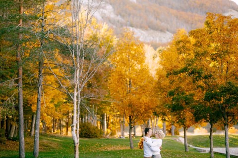 Portrait of smiling man hugging woman with wreath of yellow leaves in autumn forest.