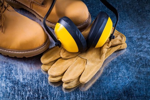 Leather safety boots gloves and noise insulation ear muffs on scratched metallic background