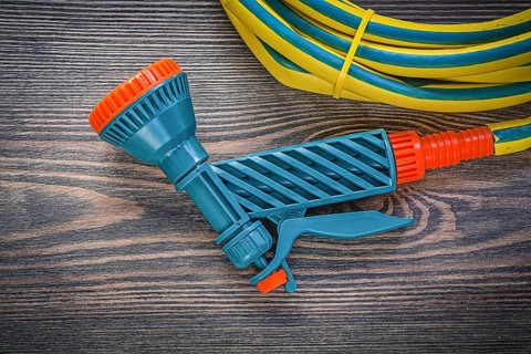 Garden hose coil water hand spray gun on wooden board agriculture concept