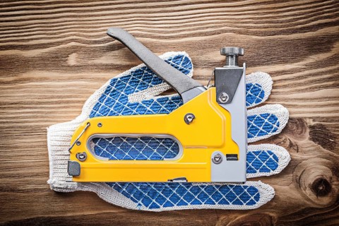 Stapler gun pair of working gloves on wooden board construction concept