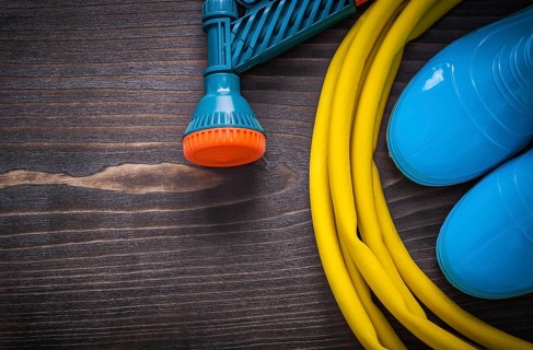 Twisted rubber hose with spray nozzle and gumboots on vintage wooden board gardening concept