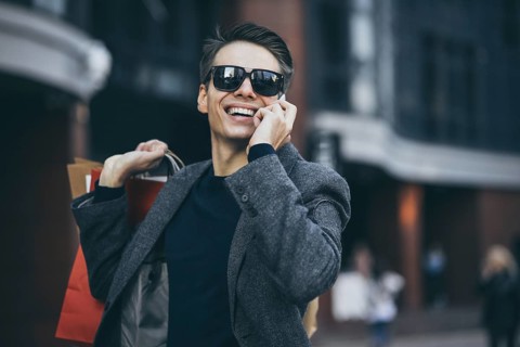 Positive cool guy with sunglasses and paper bags walking near showcase with reflection