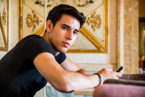 Young handsome man sitting in elegant cafeteria or restaurant using cell phone to send text message