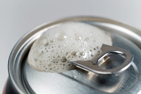 Close-up detail of a beer can with foam on a white background with space for text