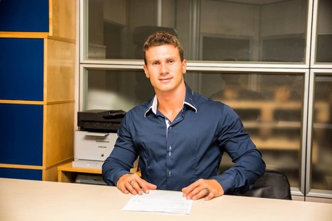 Young man standing, working in an office at the desk with a sheet of paper in front of him, looking