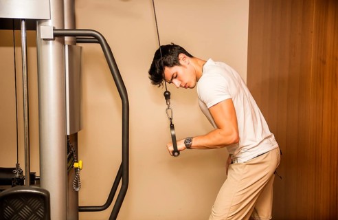 Attractive and fit young man in gym working out, doing pulley and exercising triceps on equipment