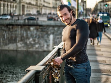 Side view of bearded man in casual clothes standing on footbridge and attaching love lock to metal