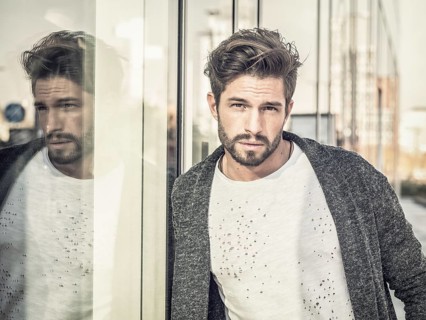 One attractive man in urban environment in city, leaning on glass shop window, wearing cardigan,