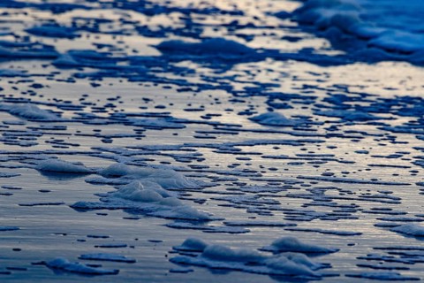 The sea waves and foam form textured patterns on the beach at dusk, Groede, Zeeland, Netherlands