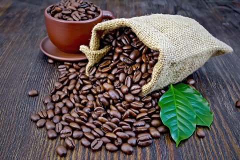 Bag of black coffee beans, brown cup and green leaves on a wooden board background