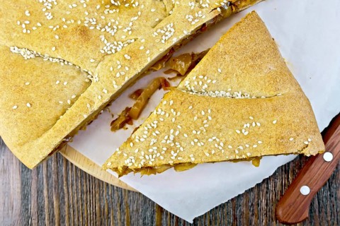 Pie with cabbage and sesame seeds with fresh rye dough knife on background wooden plank on top