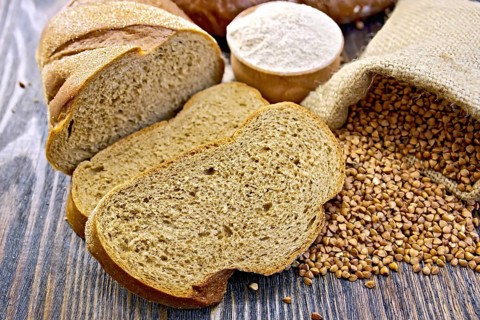 Slices of buckwheat bread, a bag of buckwheat, buckwheat flour in a bowl on a wooden boards