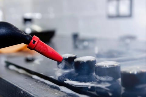 Close-up of a steam cleaner nozzle cleaning a stovetop