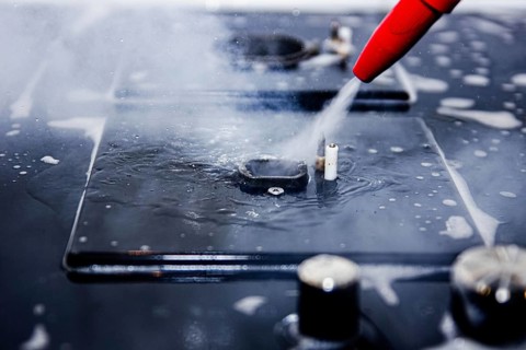 Focused image of water being sprayed from a red nozzle onto a stove