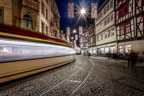 Langzeitbelichtung einer Straßenbahn, die durch eine historische Straße mit Fachwerkhäusern fährt,