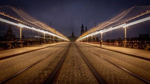 Long exposure at night of a street with fairy lights and street lamps leading to a central point,