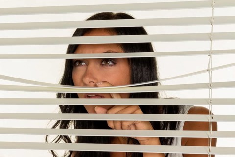 A young woman watches something through the blinds of her window Austria