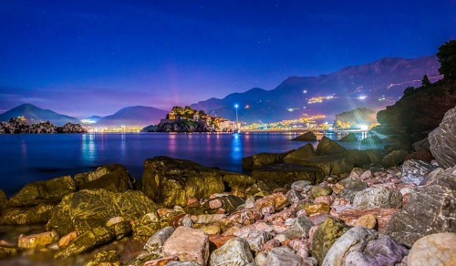 Stones on the coast of Adriatic sea near illuminated Sveti Stefan at sunset, Montenegro, Europe