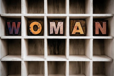 The word WOMAN written in vintage ink stained wooden letterpress type in a partitioned printer's