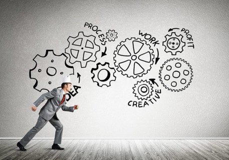 Young handsome businessman wearing white paper crown running and gear mechanism on wall