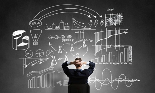 Rear view of businessman sitting in office chair and looking at infographs on chalkboard
