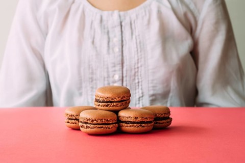 Macaroons on heap on pink table against woman. Selective focus