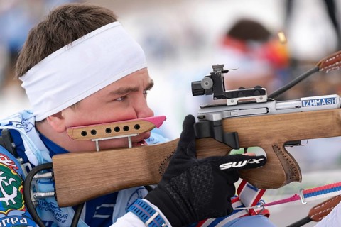 Close-up view of sportsman biathlete aims rifle shooting prone position. Biathlete Andrey Krutov in