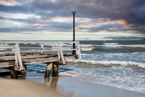 Storm sea waves empty wooden pier in dramatic blue sky background. Seascape with running splashing