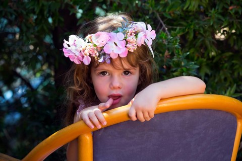 Happy childhood concept. Charming curly little girl in a wreath of flowers resting in a chair in
