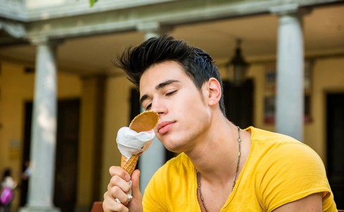 Funny attractive young man sitting, wearing yellow T-shirt while eating a tasty vanilla ice cream
