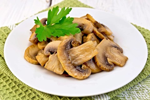 Champignons fried in a plate with a leaf of parsley on a napkin on the background light wooden
