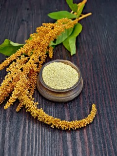 Groats amaranth in a clay bowl, brown flower with green leaves on a background of wooden boards
