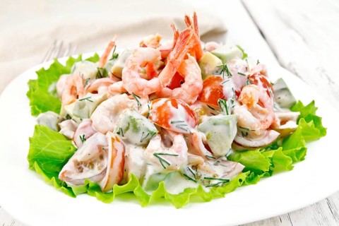 Salad with shrimp, avocado, tomatoes and mayonnaise on the lettuce in the plate, napkin, fork on