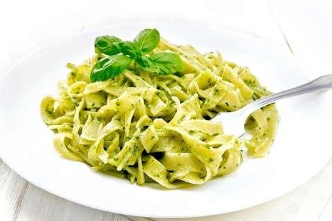 Tagliatelle pasta with pesto, basil and fork in a plate on a napkin against the background of light