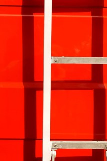 Close-up of the body of a fire engine in the sunshine with a ladder casting a shadow