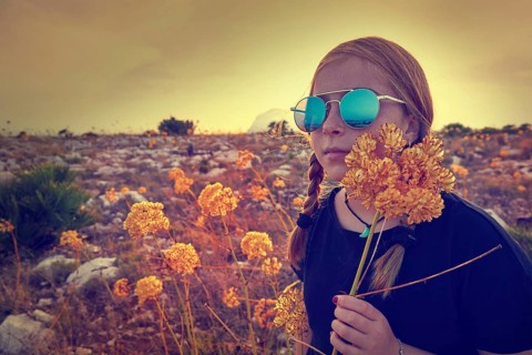 Blond country girl with sunglasses and flowers at sunset outdoor mountain