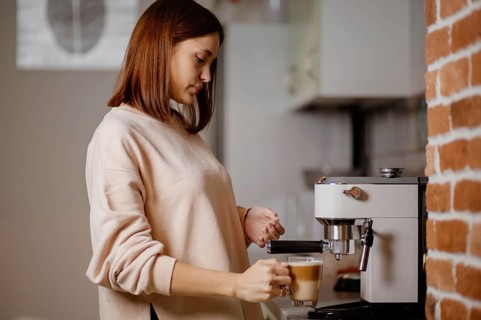 Woman adding milk to coffee using an espresso machine in the kitchen