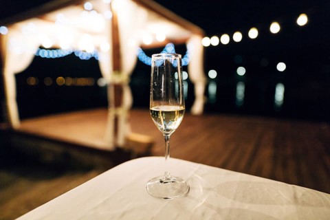 A glass of champagne stands on the table against the backdrop of a party on the beach. Beach talk