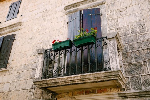 Stone balcony with a wrought iron lattice with flowerpots on the stone facade of the house.