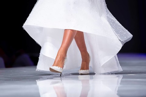 Female model walks the runway in white dress during a Fashion Show. Legs and shoes only. Fashion