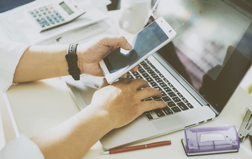 Businessman hand using smart phone and keying the data to laptop, mobile payments online shopping