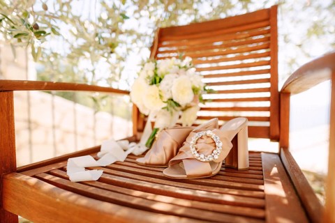Close-up of a wooden chair with a round buckle clog and a bouquet of flowers under an olive tree.